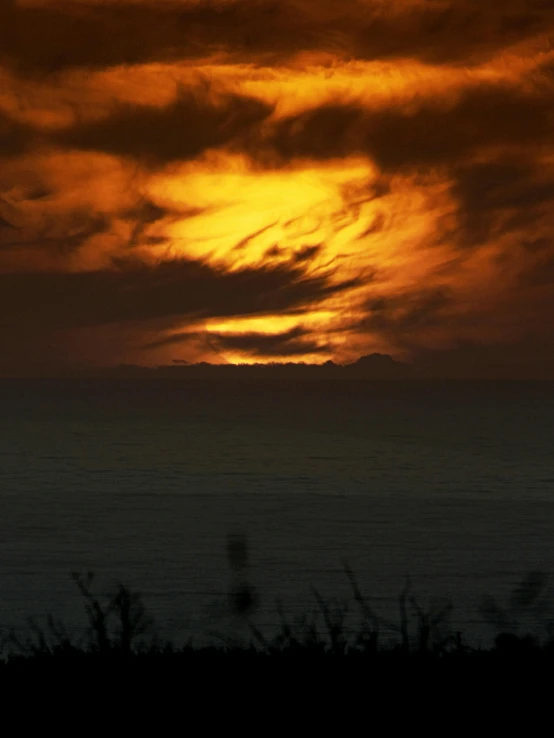 a sunset seen over the water and clouds over land