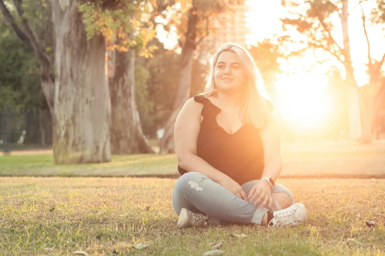 a woman sitting on a field with trees in the background