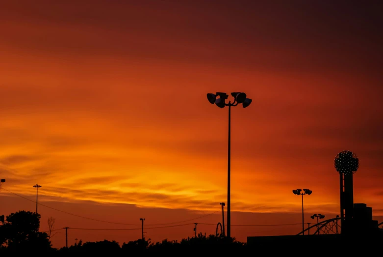 a sunset with clouds and street lights near a park