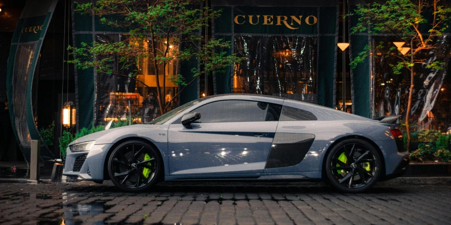 the front end of a silver sports car in front of a building at night