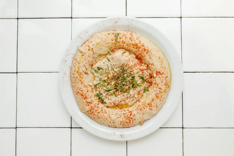 a plate with hummus and garlic on it sits on a tile surface