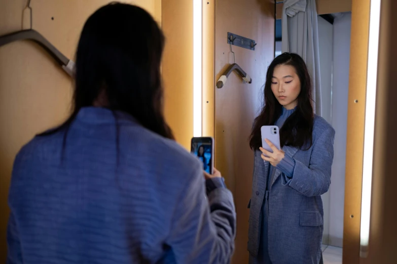 a woman looking at her cell phone in the mirror