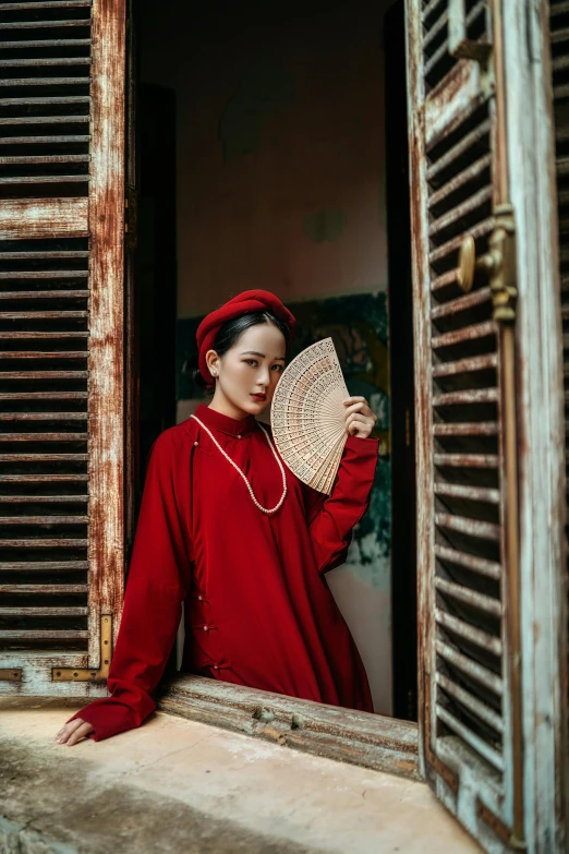 woman in red, with a fan sitting by the window