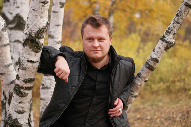 a man leaning against the trunk of a birch tree