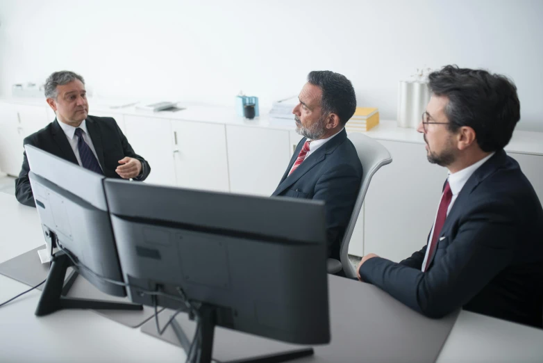 two men talking at a computer while the one has his hand on the monitor