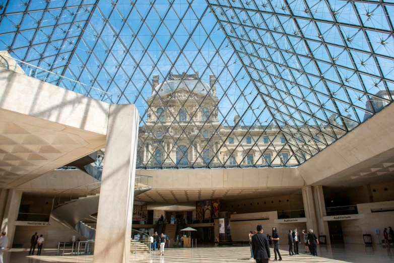 people walk around inside of a museum with a tall glass roof