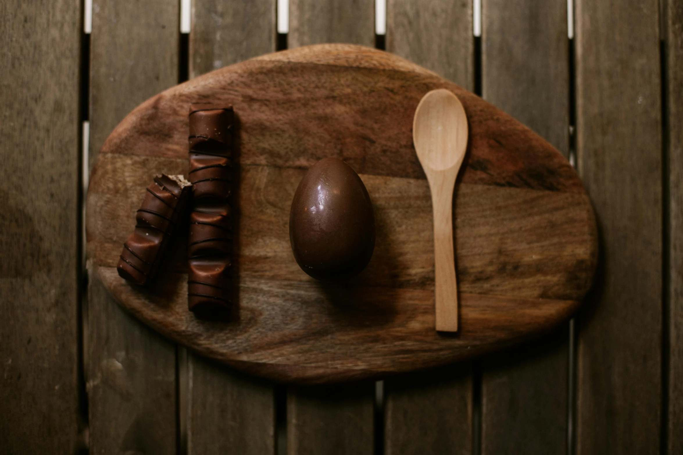 an egg, chocolate, and spoon are on a wood board