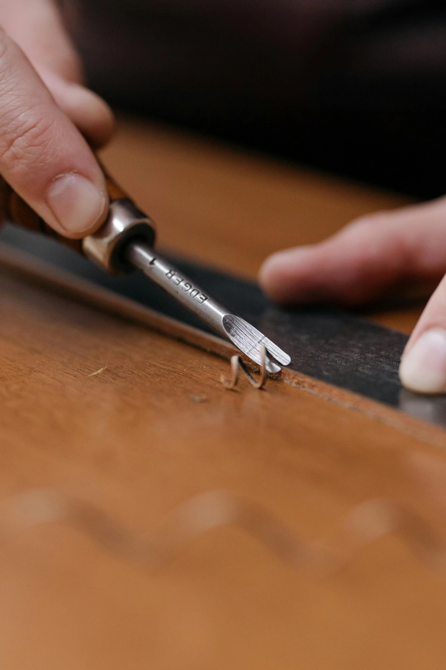 a pair of hands sharpening a metal blade on a piece of wood
