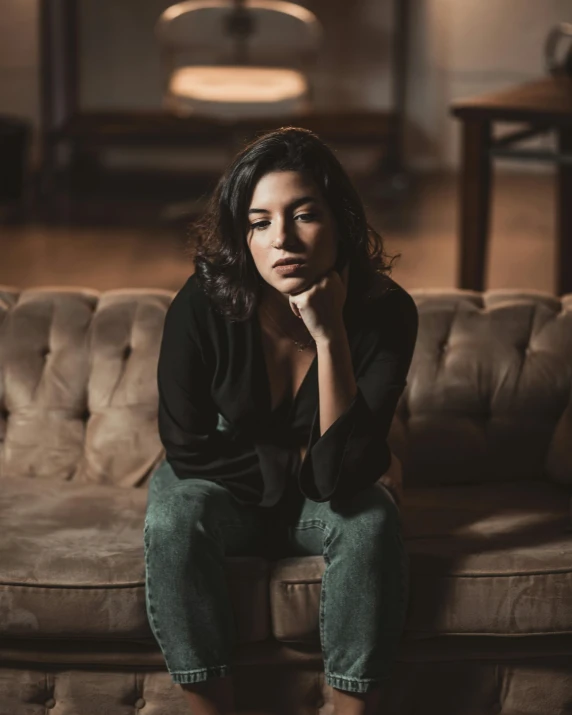 a woman sitting on a couch with her chin resting her hand on her cheek