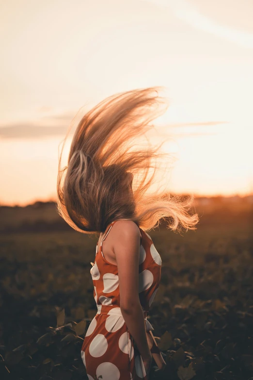 a girl walking across a field with a wind blowing her hair