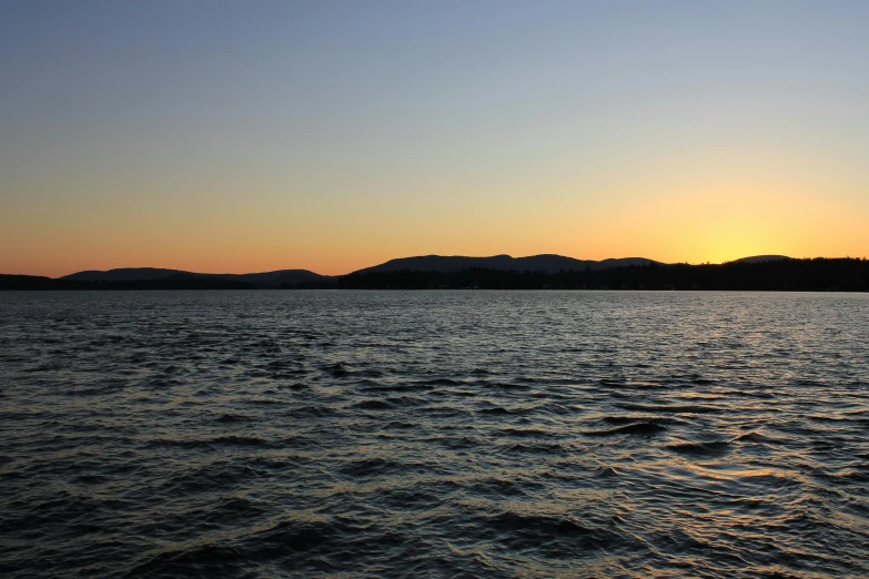 the sun is rising over a body of water with hills in the background