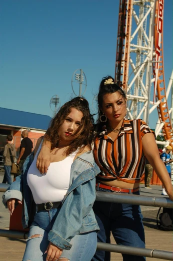 two women in jeans are standing by a ferris wheel