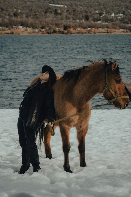 a woman in a black outfit is standing next to a brown horse