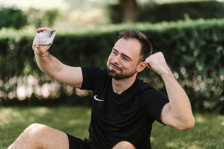 man sits outside while holding up a small white cell phone