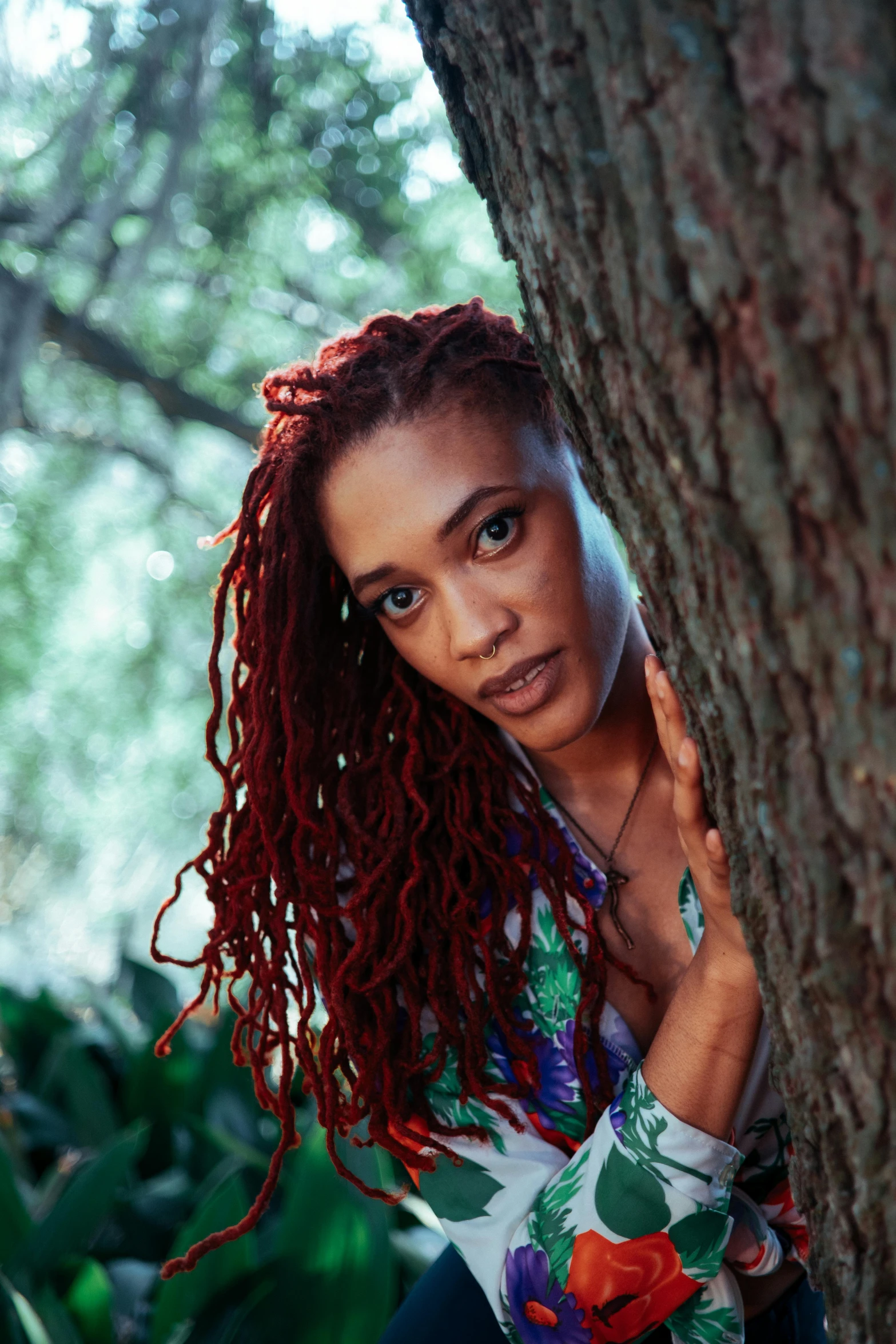 a girl with long, red hair leaning against a tree