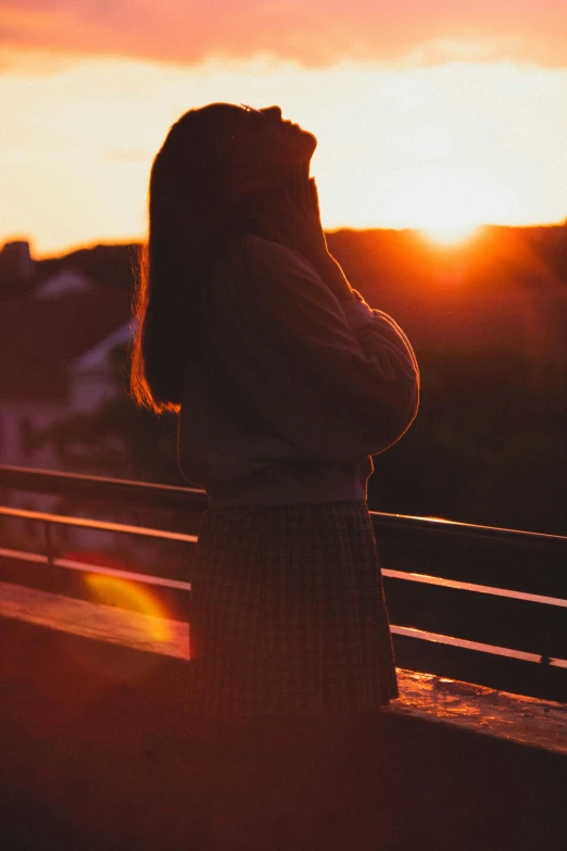 a woman standing outside at sunset with her hand on her cheek