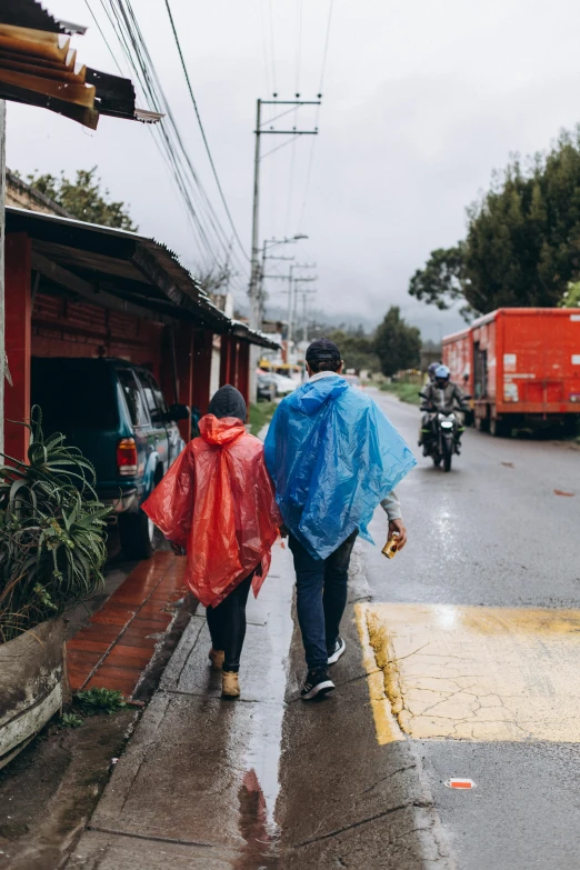 two people walk in the rain near a red building