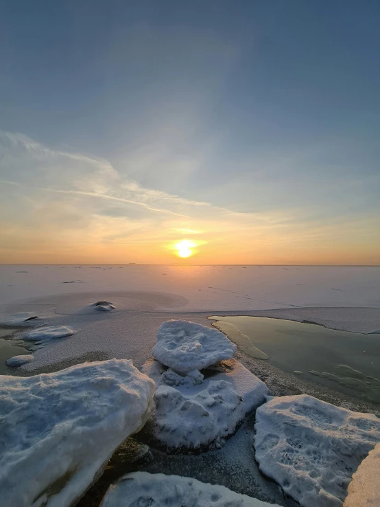 a sun setting over the ocean and snowy landscape