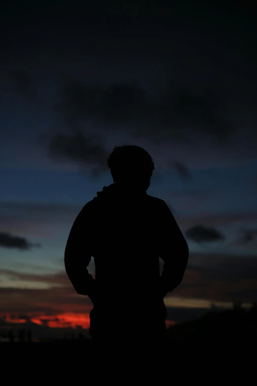 the silhouette of a person looking back at the sunset