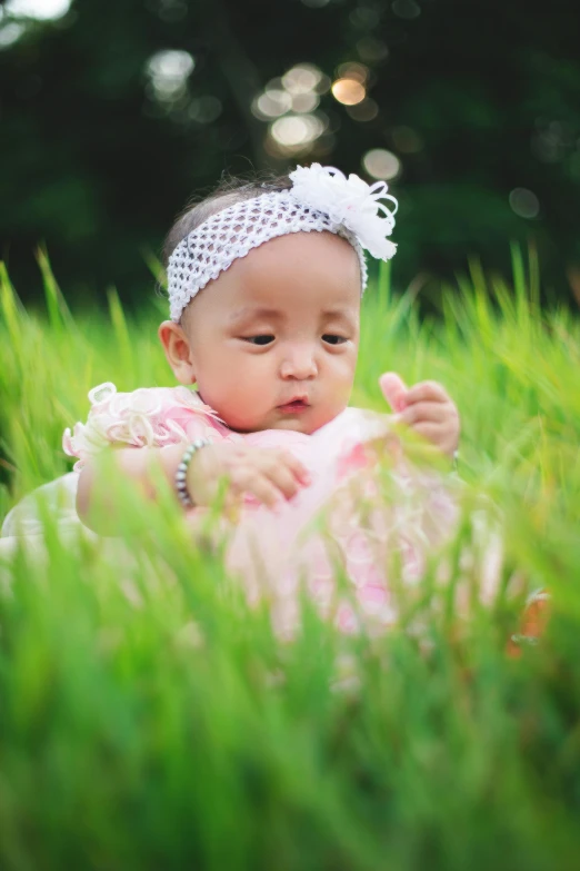 a baby sitting in the grass with her head in her hand