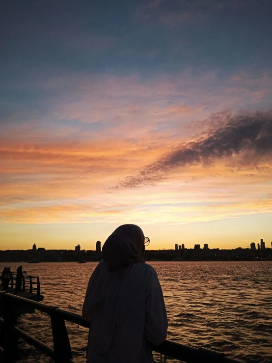 a woman standing next to the water watching a sunset