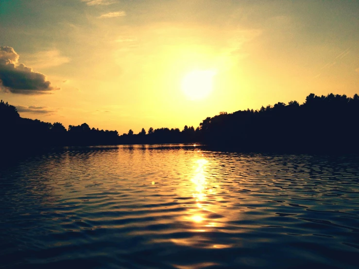 the sun shining over some trees on a body of water