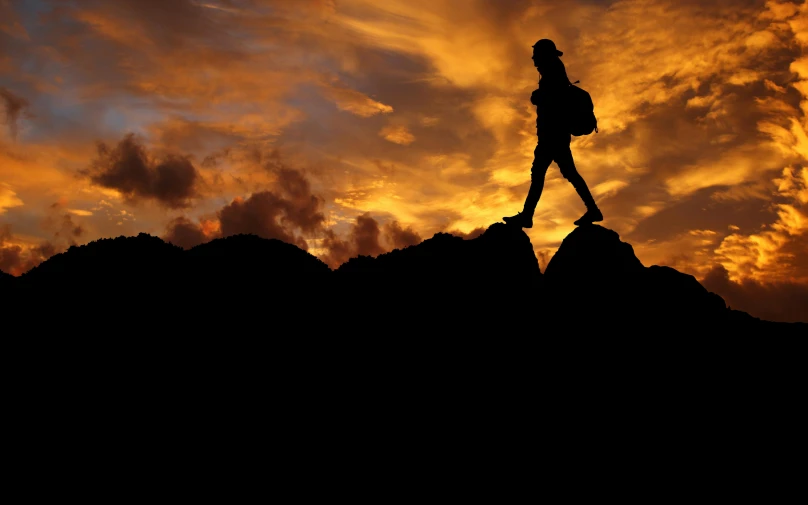 a silhouette of a person walking over a hill at sunset