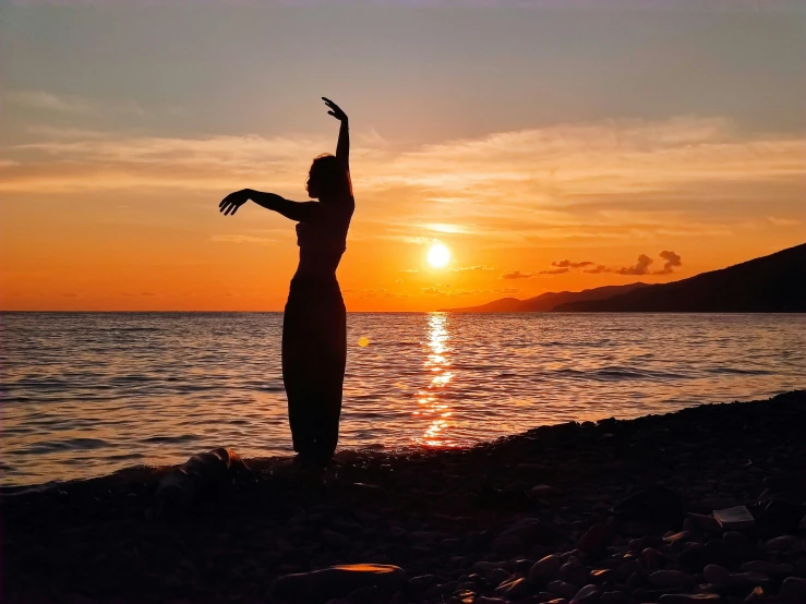 a woman standing on the beach at sunset in a black dress