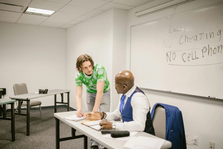 two men sit at a desk and look over papers