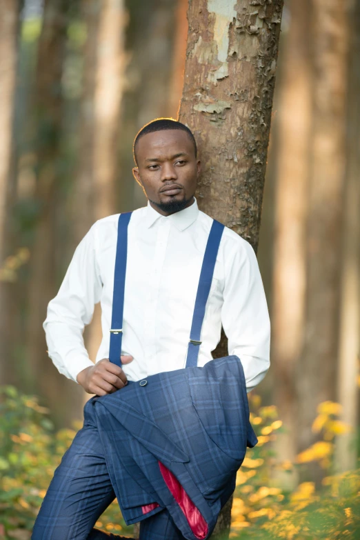 a man wearing suspenders and a white shirt standing next to a tree