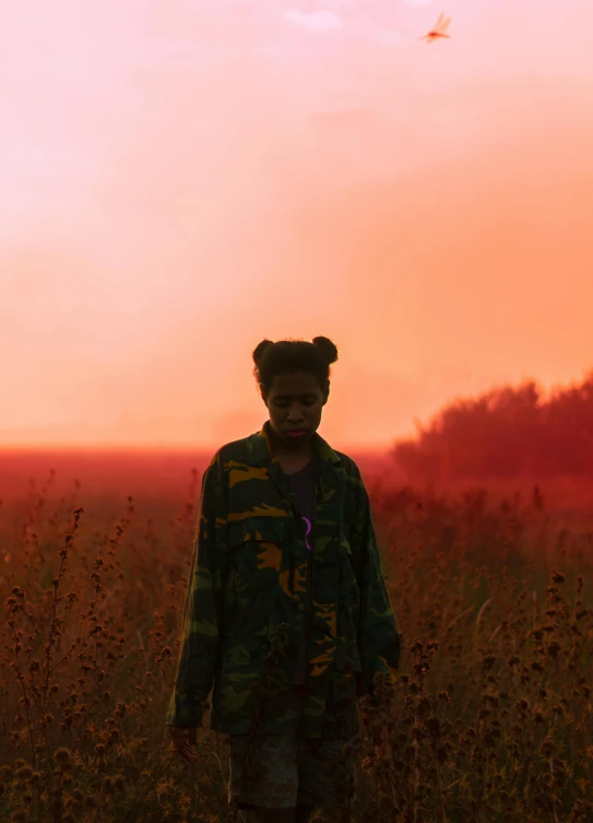 a boy standing in a field while the sun goes down