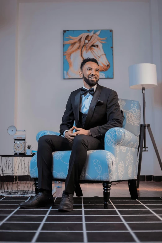 a man in a tuxedo sitting on a blue chair
