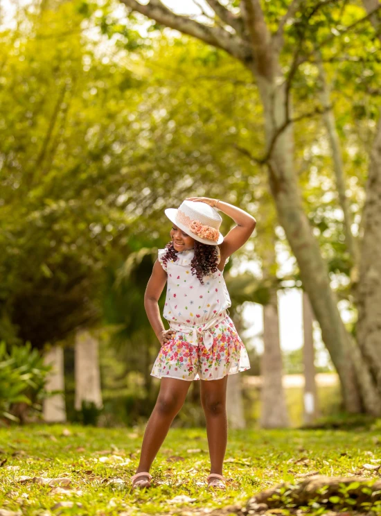 little girl in white dress and pink hat standing by trees