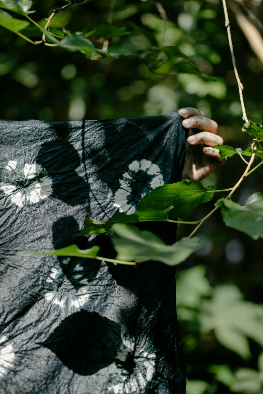 a woman holding a large piece of umbrella in front of green leaves