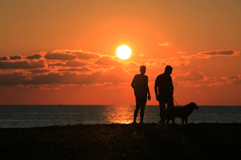 the sun is rising with two people with their dogs