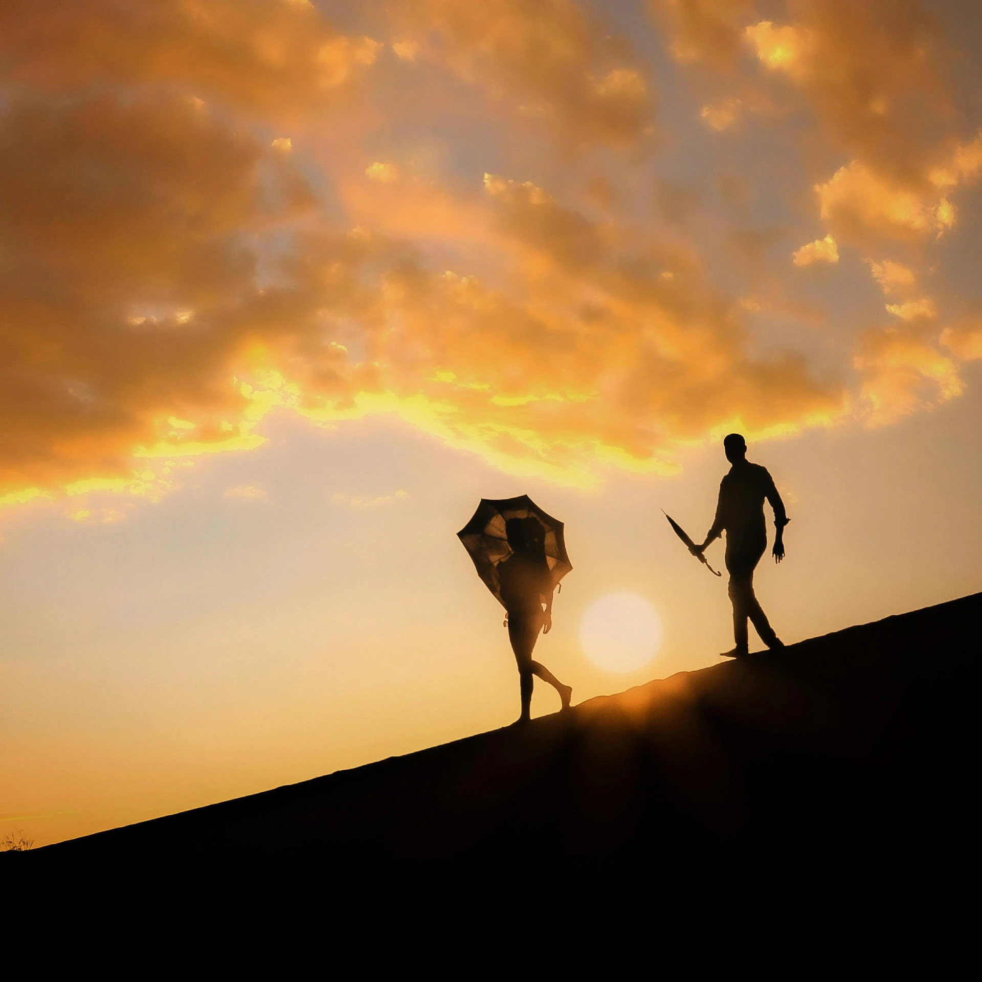 two people walking down a hill at sunset with an umbrella