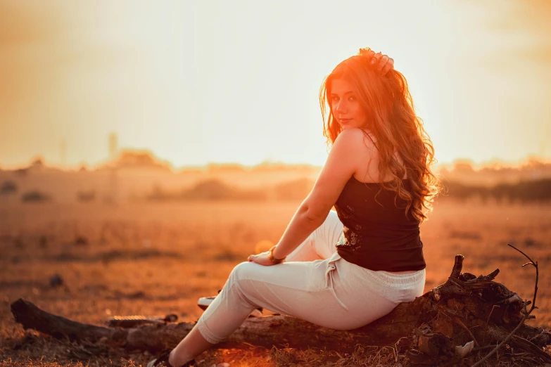 a woman is sitting in a field near a fallen tree