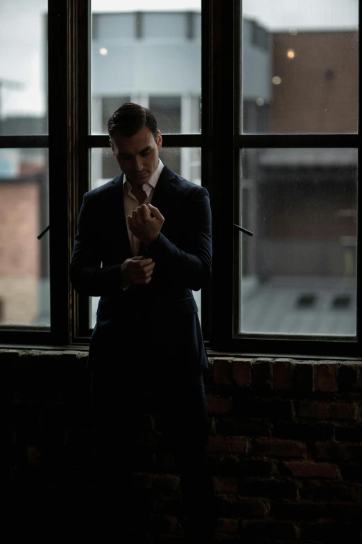 man in a suit looking outside a window while holding a white paper