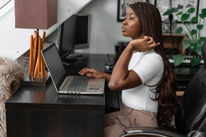 a woman with cornrows sitting at a desk with a laptop