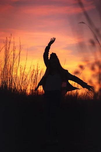 a woman raising her arms up while a setting sun looms over the horizon