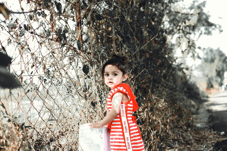 a little girl stands outside in front of a bush