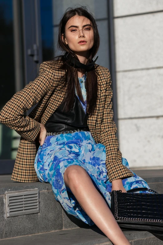 a woman sitting on a wall in front of a building wearing a blue floral skirt