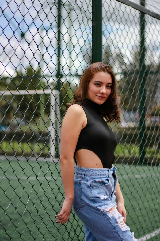 a woman in high waist jeans and crop top standing against a fence