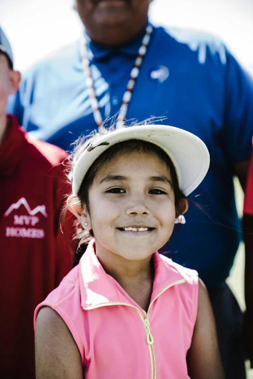 a smiling little girl is in a pink shirt and hat