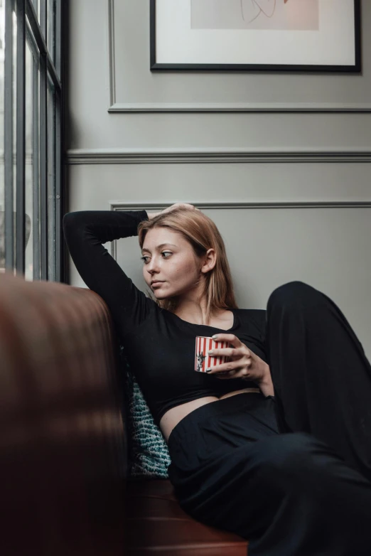 a pretty young woman laying on a couch holding a cup of coffee