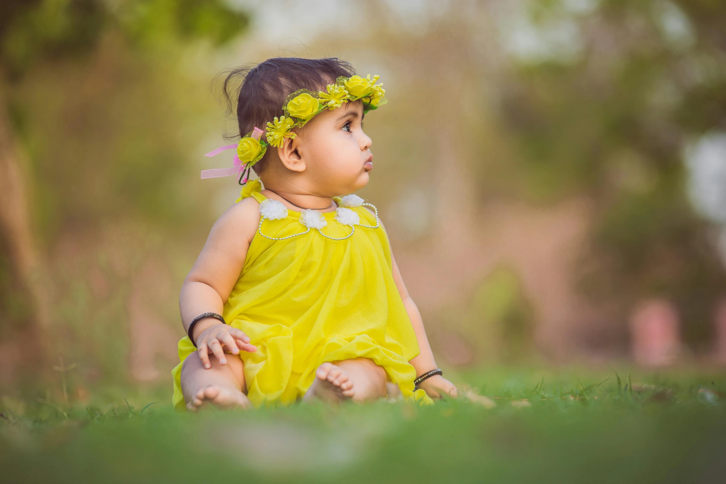 a baby girl in a yellow dress sits in the grass