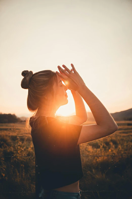 woman standing in field looking up at the sun