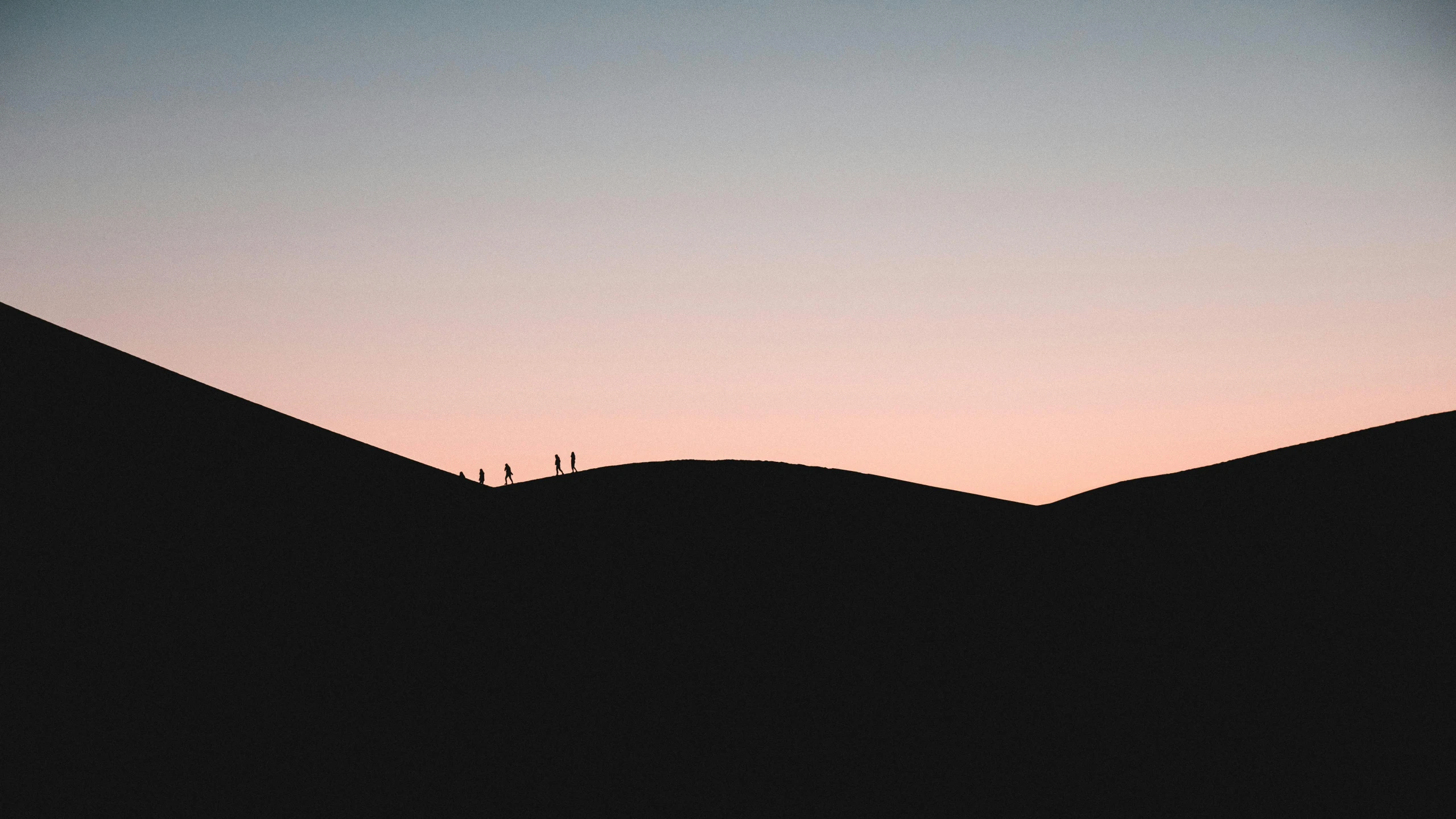 people are walking across the desert at dusk