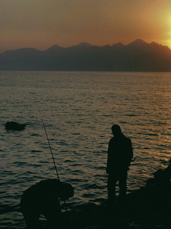 a man standing on the edge of a cliff with two dogs watching the sunset over some water