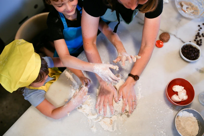 a woman helping two children with kneads in dough